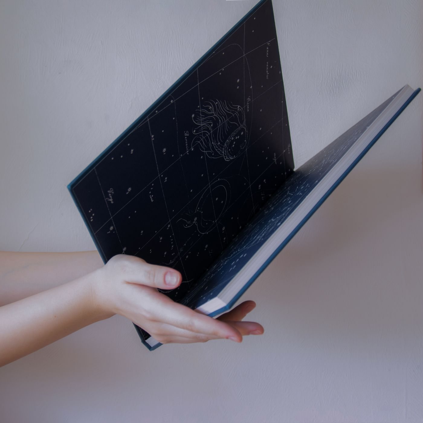 Hands holding a book showing celestial charts