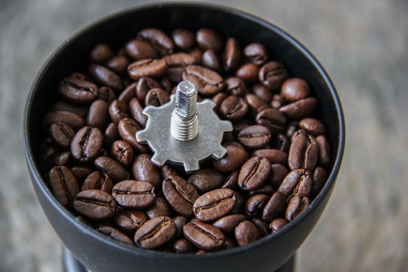 Roasted coffee beans beside a hand coffee grinder