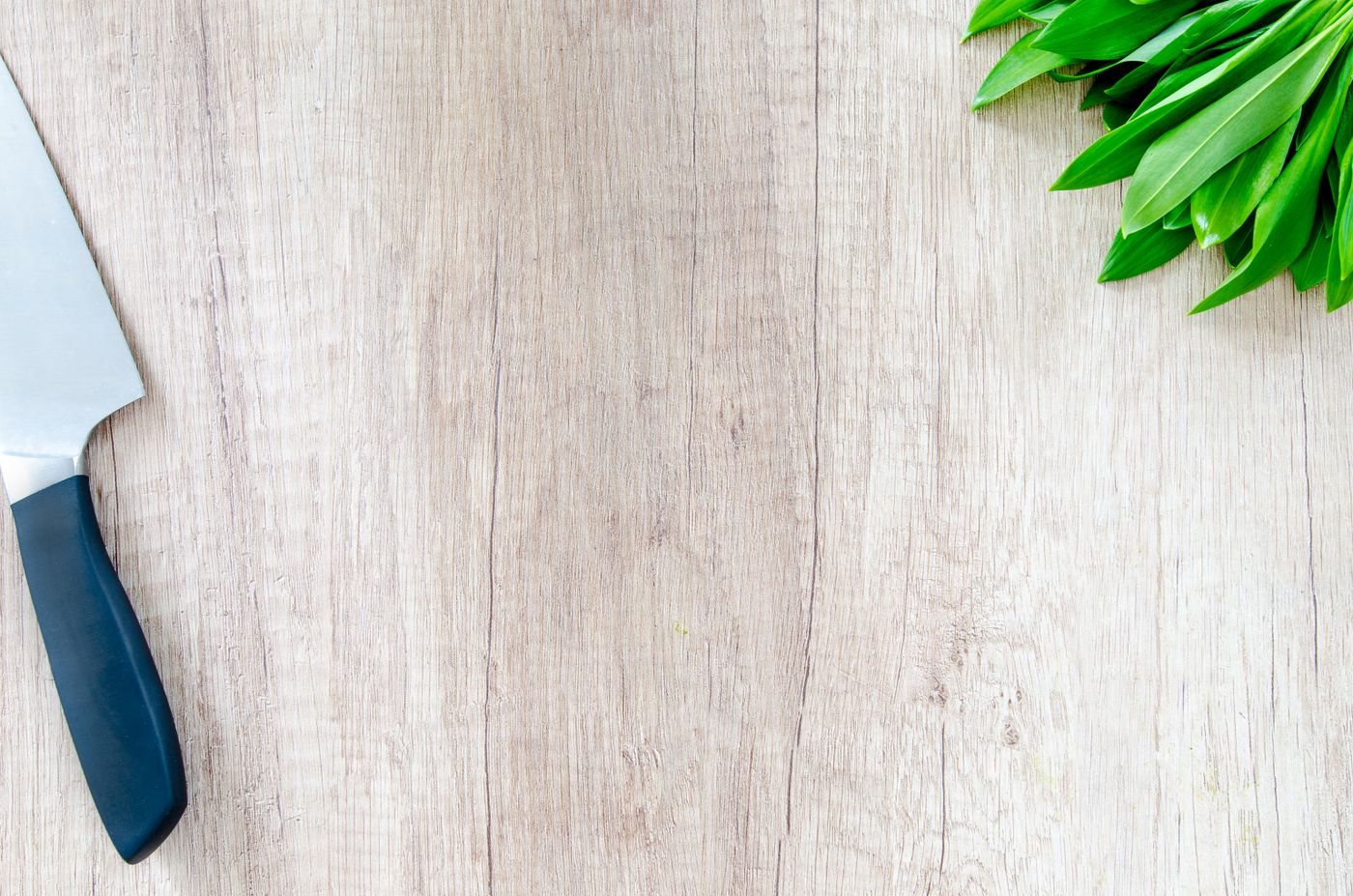 A kitchen knife and fresh herbs on a wooden surface