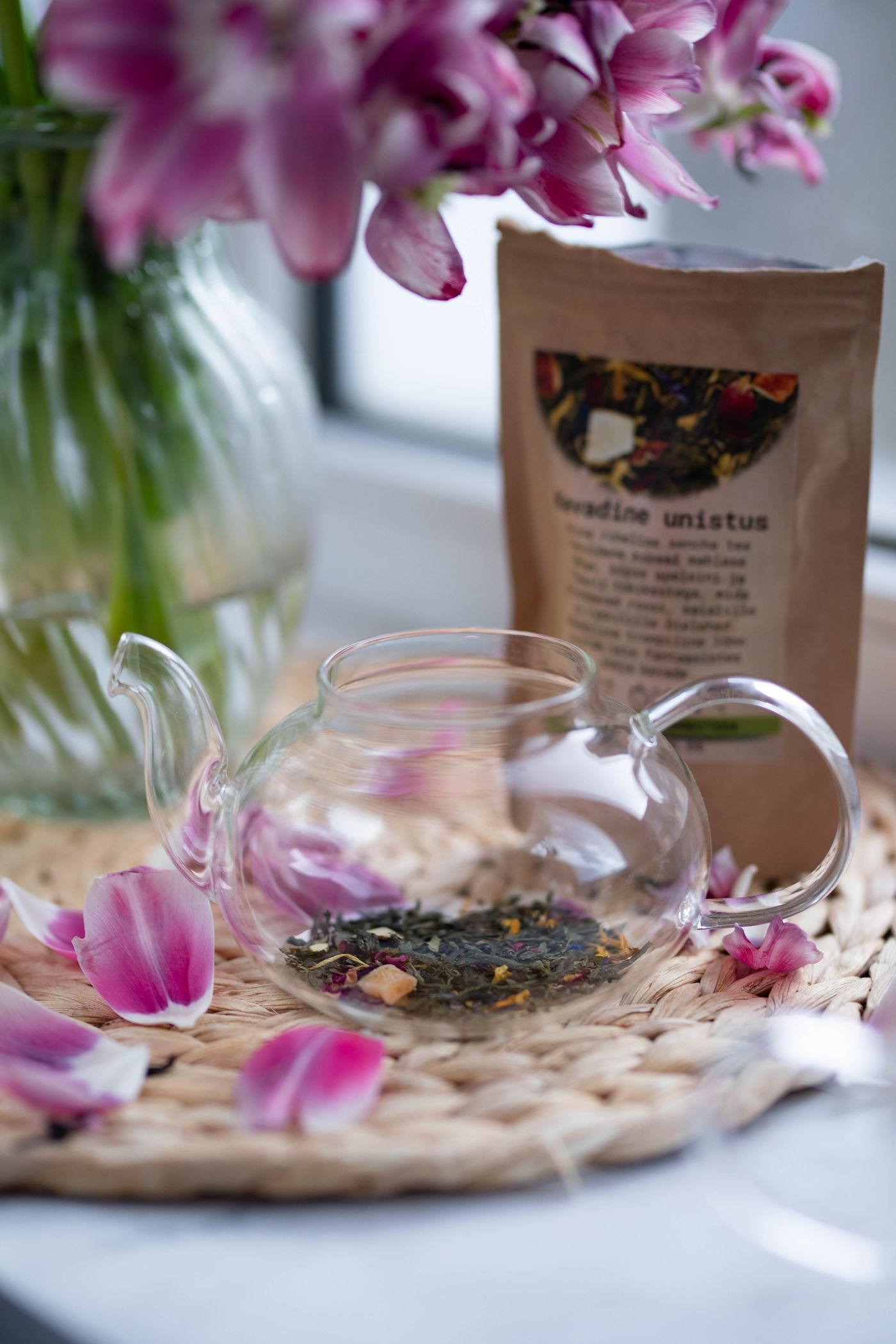A glass teapot with loose tea on a woven mat