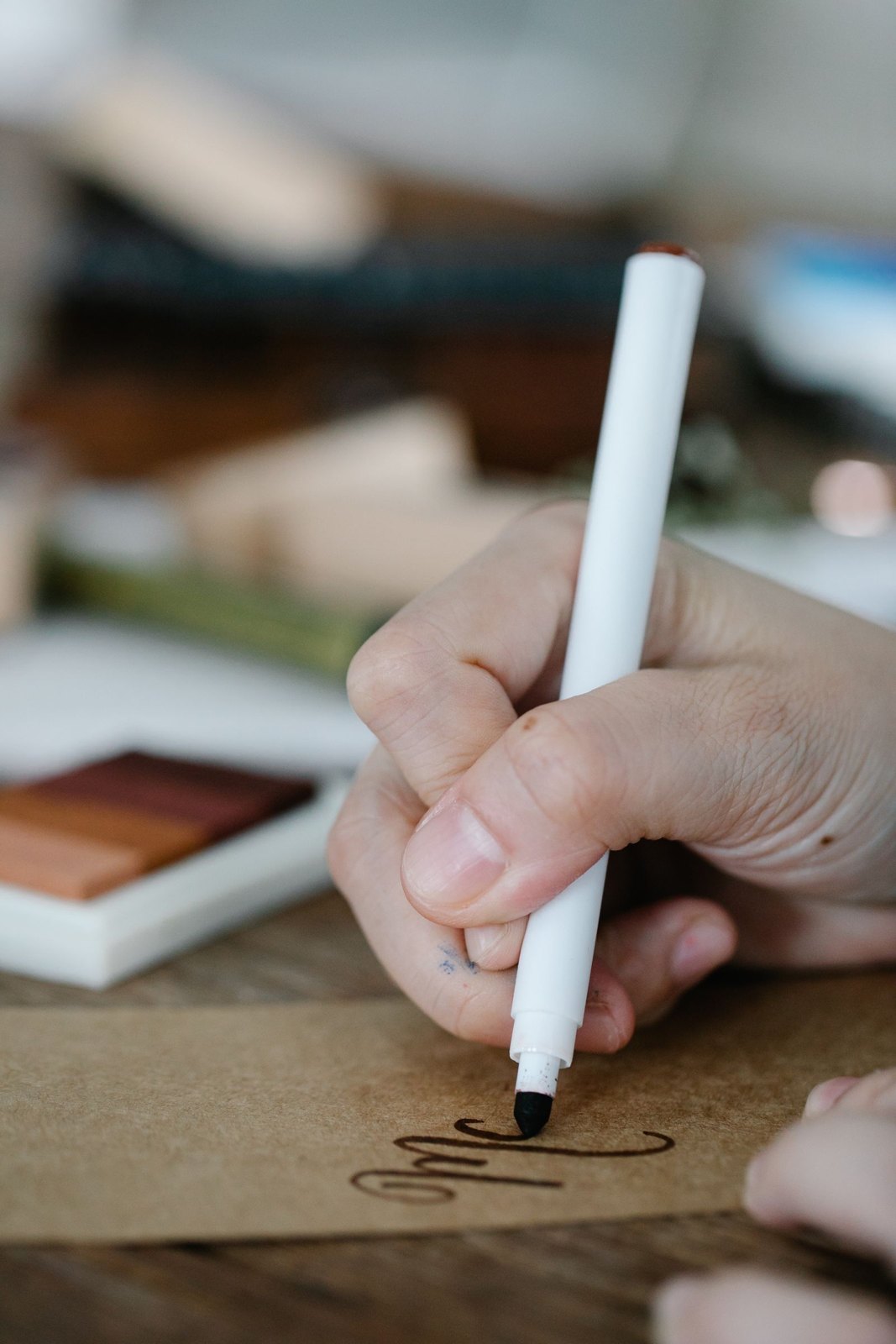 A hand lettering a message on a brown card